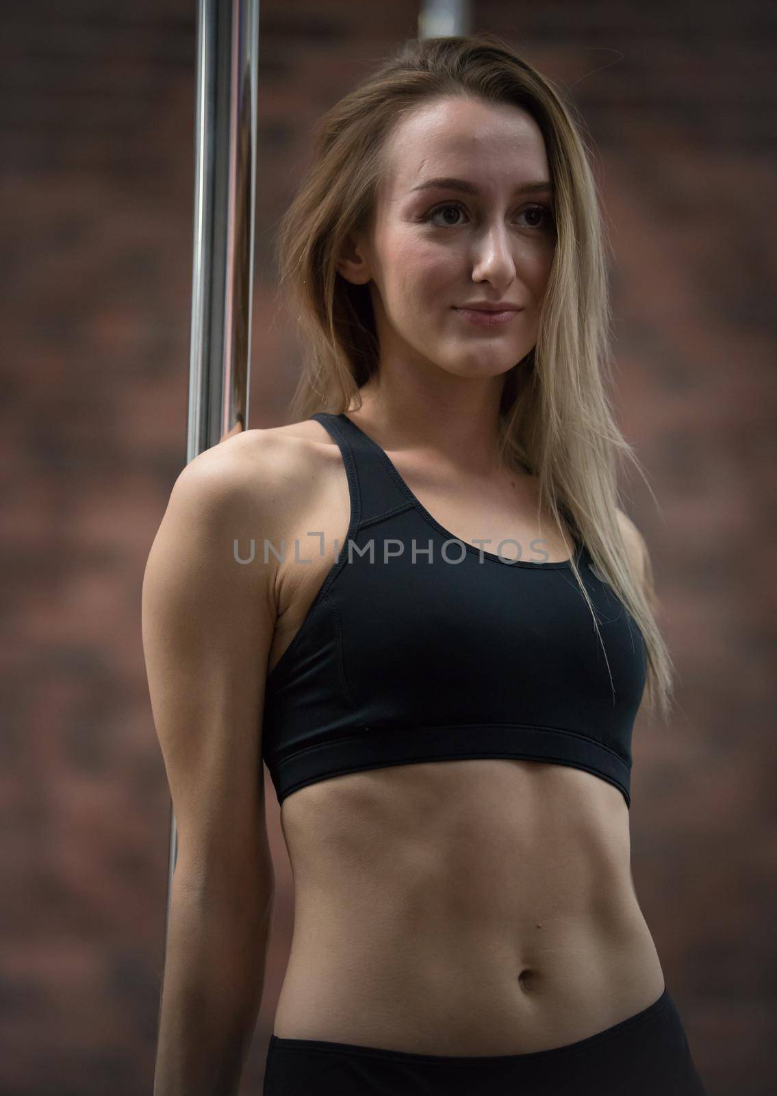 Young pretty woman in sport bra staying next by the pole. Portrait