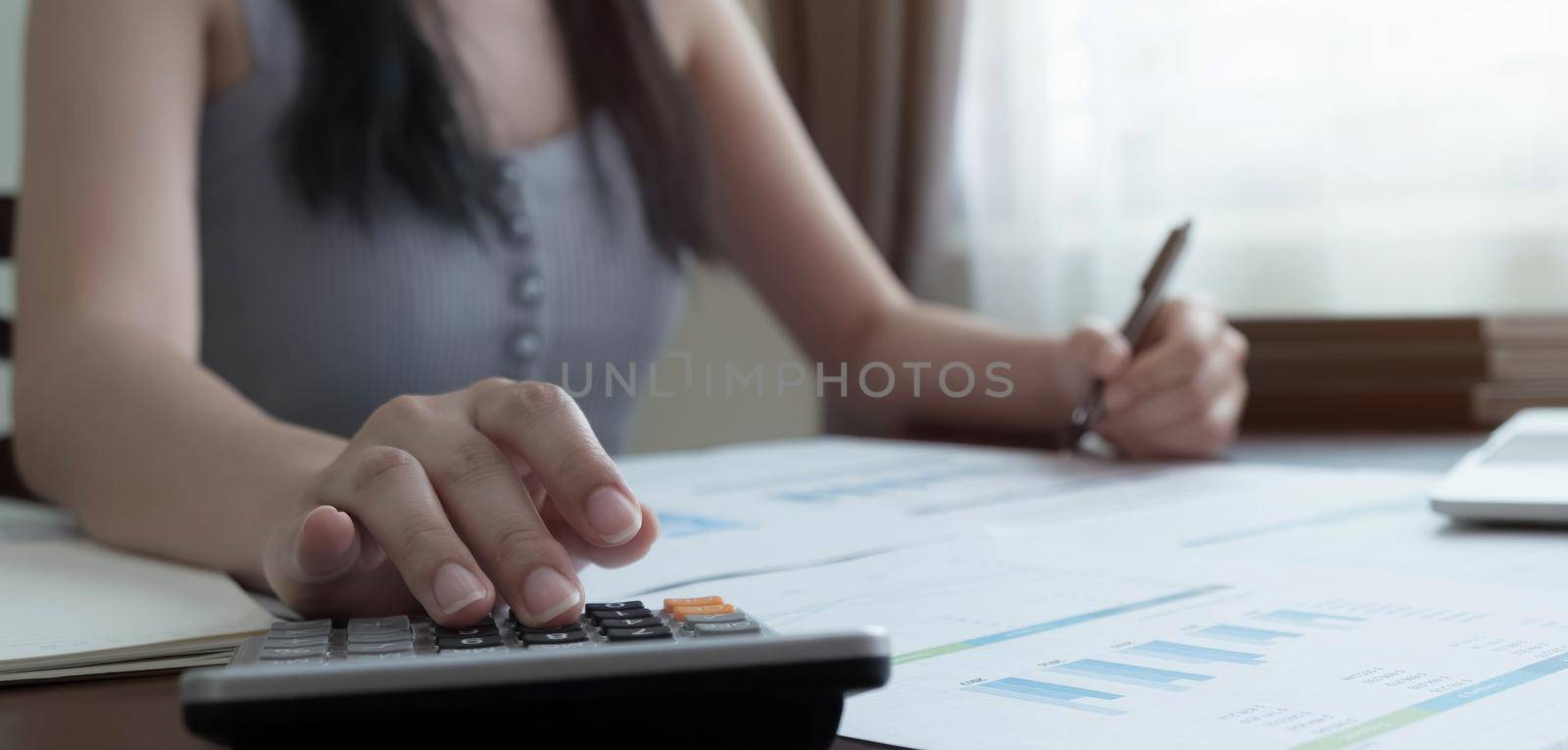 Close up woman using calculator and laptop for calaulating finance, tax, accounting, statistics and analytic research concept by wichayada