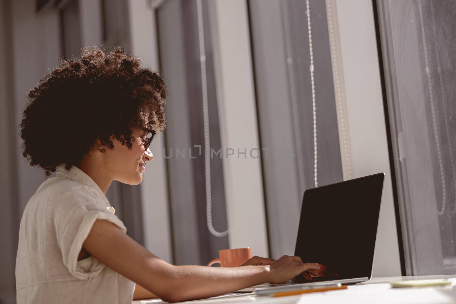 Smiling female assistance sitting at workplace while typing on laptop near the window