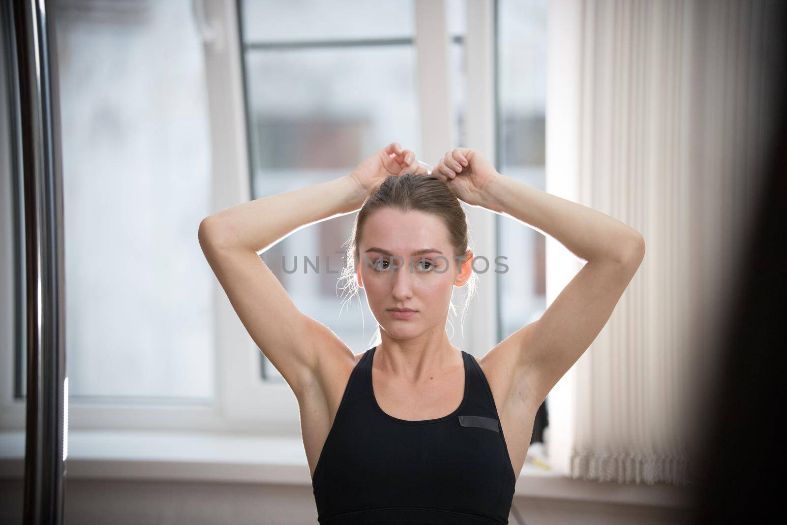 Young attractive woman in sport bra in training studio puts her hair in ponytail. Portrait