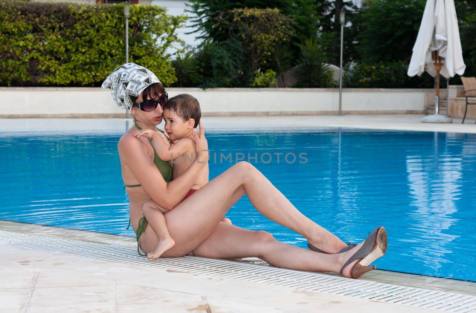 Happy family and healthy lifestyle. Young mother with small child near the pool are resting at the resort