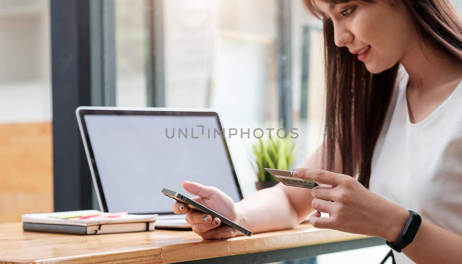 Online shopping concept, young woman hands holding using mobile smart phone and credit card making online payment with laptop computer on table while holiday.