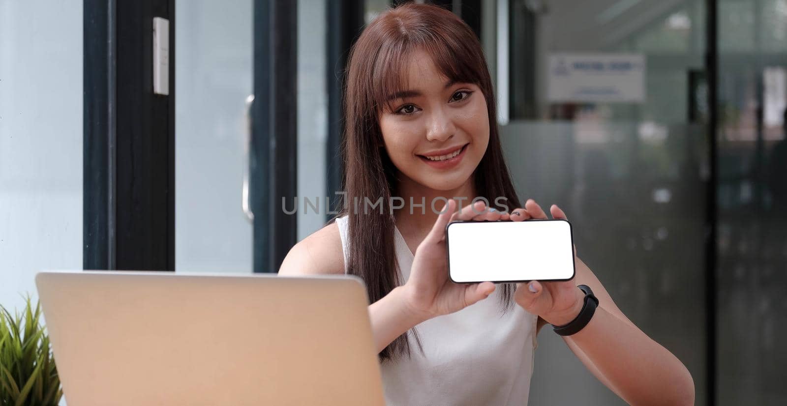 smiling happy woman in casual showing blank smartphone screen while looking at the camera isolated over white background. Using phone..