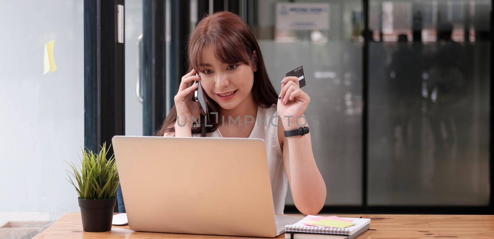 Smiling woman sitting office talking on mobile phone making online payment on her tablet computer.