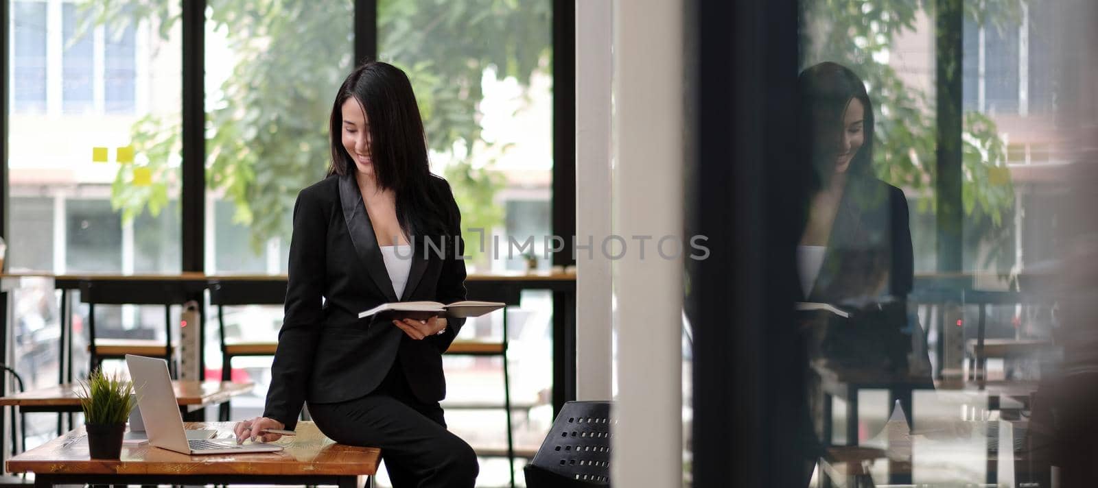 Portrait of successful young Asian businesswoman at office, Smart woman sitting on desk and working with laptop computer.