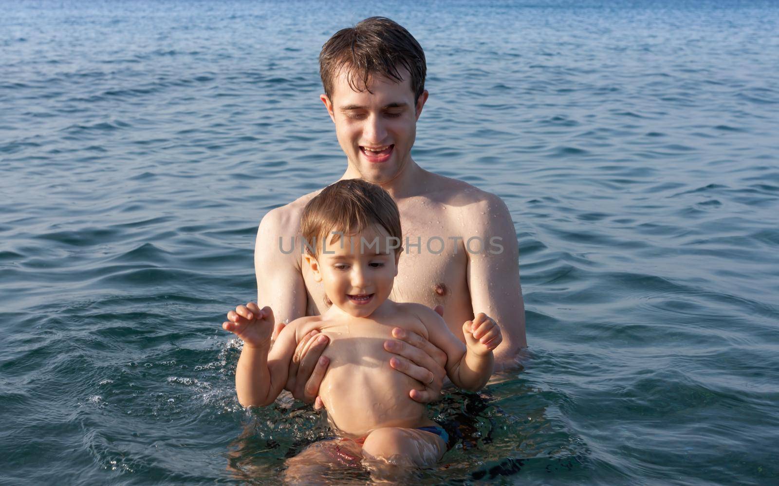 Happy family and healthy lifestyle. A young father teaches a child to swim in the sea