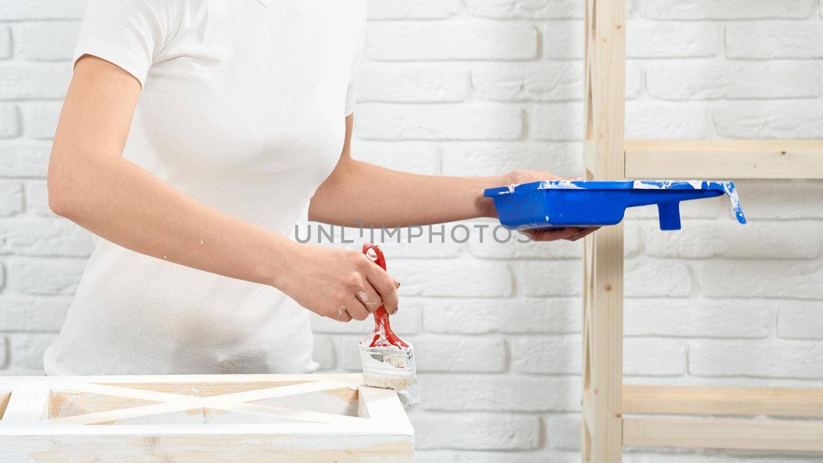 Close up of woman painting wooden shelves with white color by SerhiiBobyk