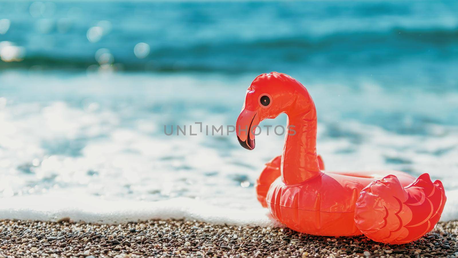 inflatable flamingos on beach with sea wave by fascinadora
