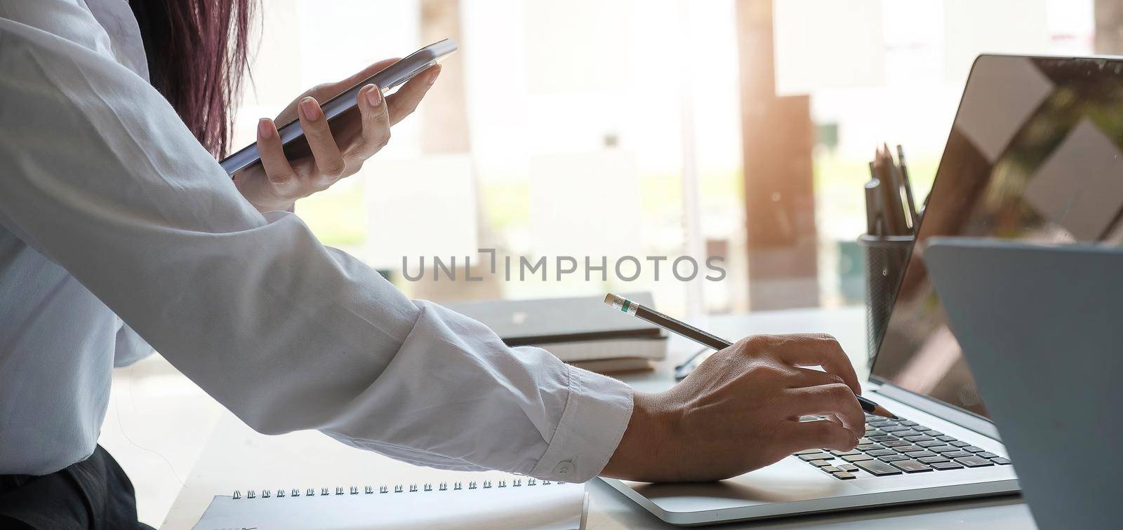 Business women hand are uses a smartphone and use a laptop computer in office..