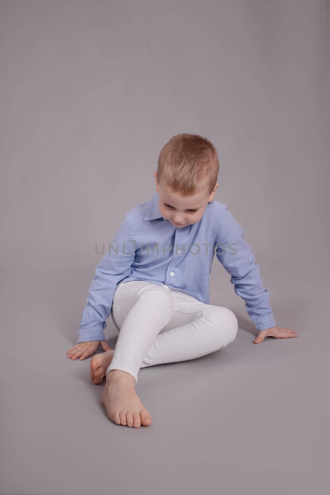 charming little preschool boy in white pants and blue shirt on gray background. child, kid.