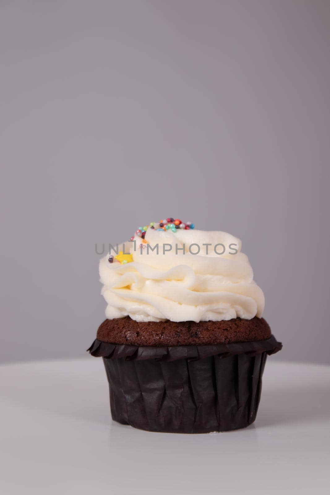 tasty chocolate cupcake with white topping cream on a white stand on a gray background. sweets, bakery. party food. dessert by oliavesna