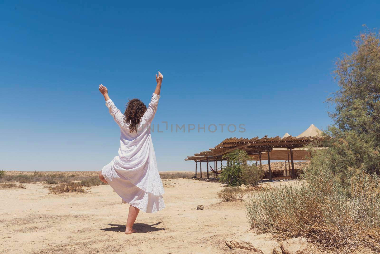 A woman stands in the desert and looks at the horizon. White clothing fluttering in the wind. Concept for relaxation, inner looking, meditation, peace of mind. High quality photo