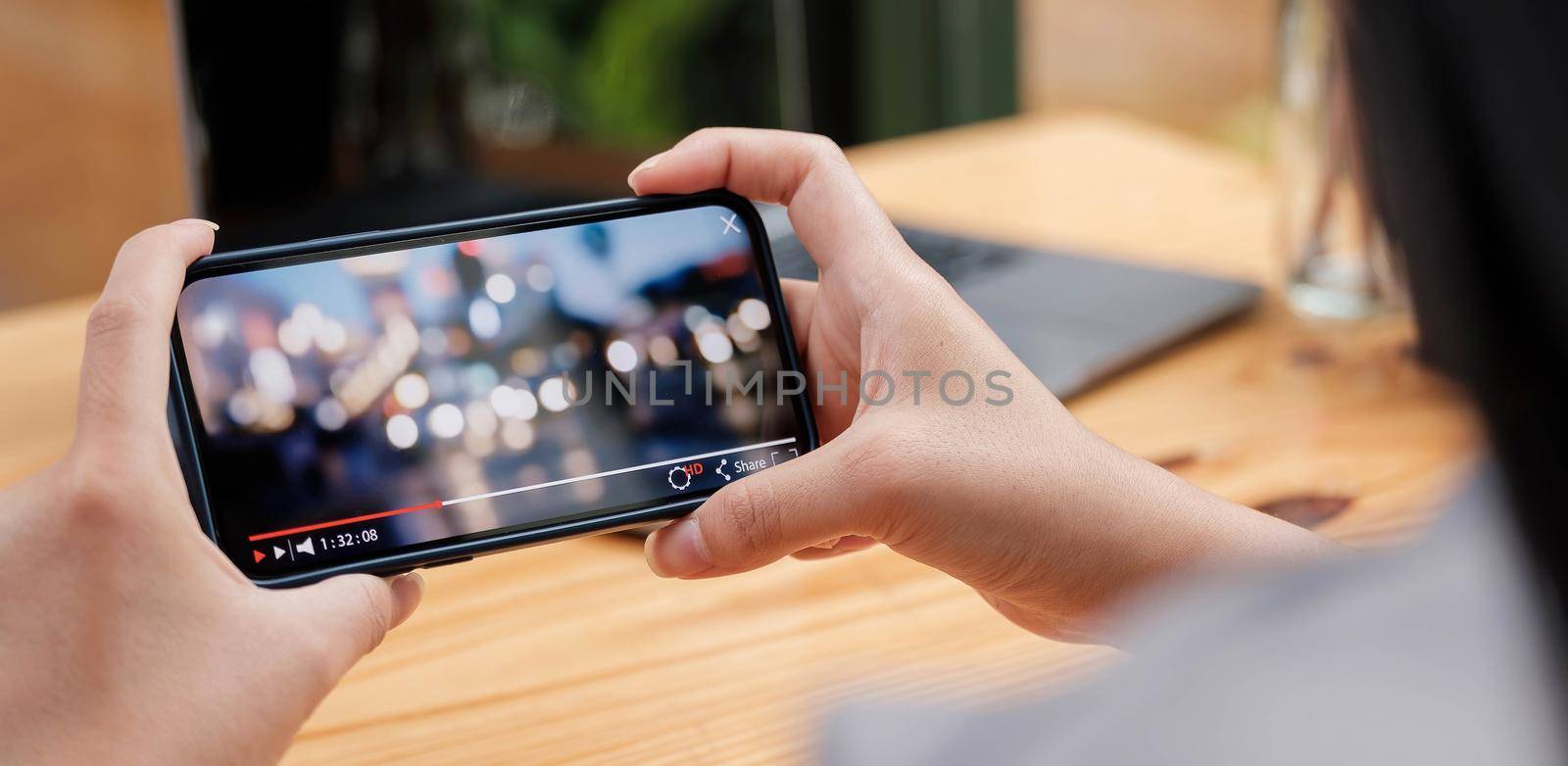 Cropped image of female hand holding smartphone and watching video while standing outdoor. by wichayada