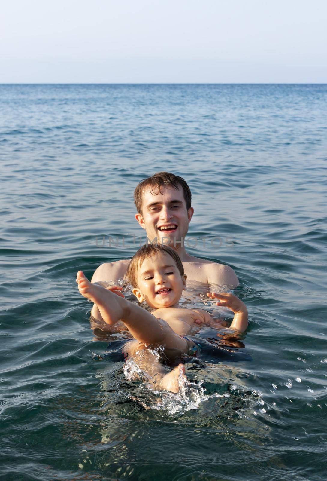 Happy family and healthy lifestyle. A young father teaches a child to swim in the sea