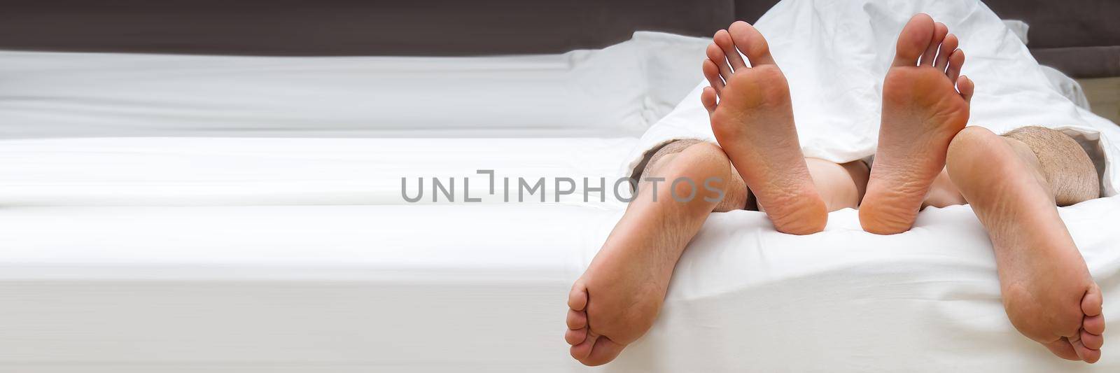 Lovers feet touch having sex on white linens in bedroom, sensual couple enjoy intimate moment relaxing in bed in man on top position. close-up