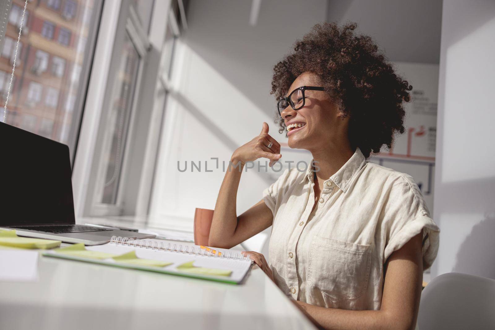 Happy woman communicating in sign language online at a laptop from office while sitting near window