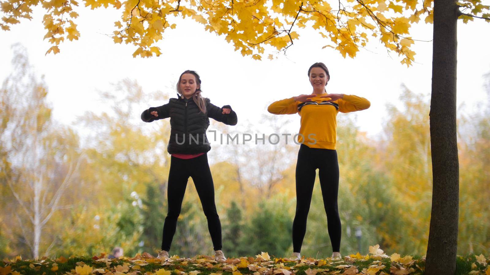 Acrobatic girls in jackets warming up outside before training in park. Hands to the sides. Autumn