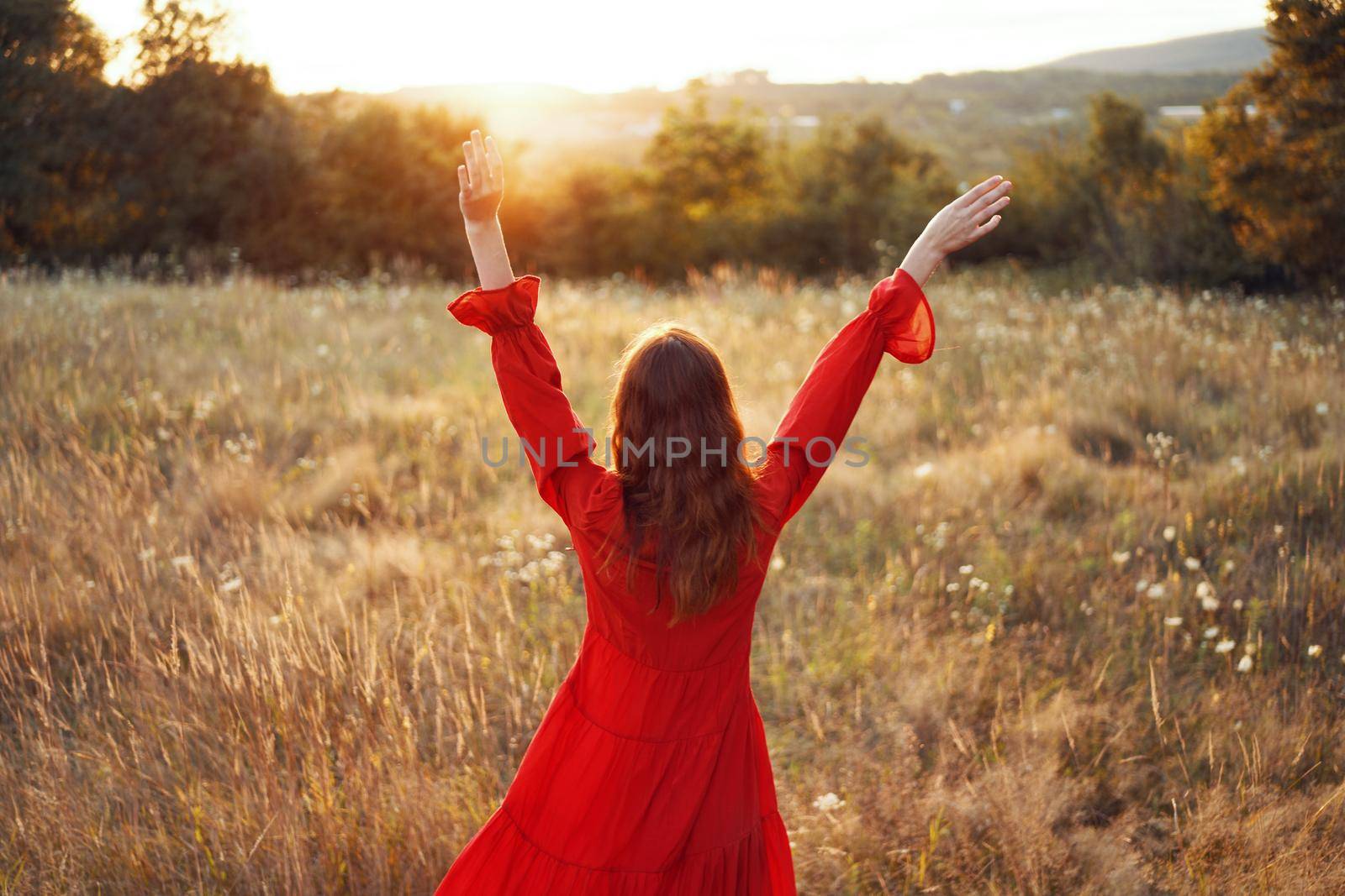 woman in red dress in the field with hands raised up posing. High quality photo