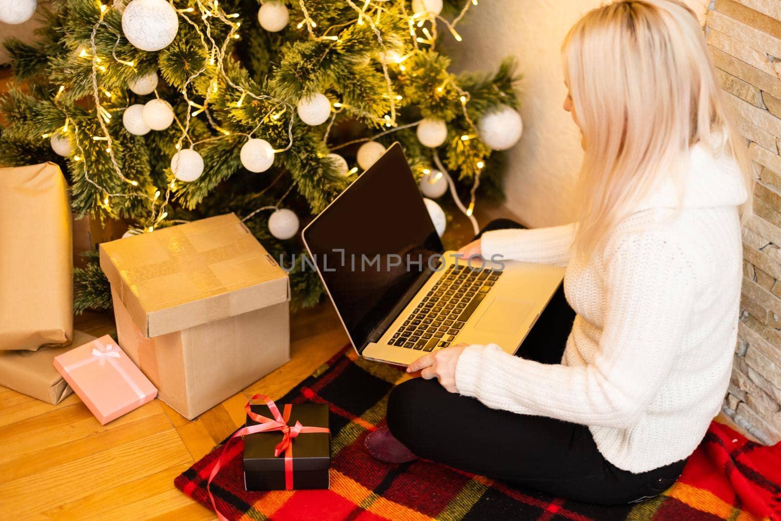 Photo of a beautiful blond female sitting on a couch using a laptop to shop for Christmas gifts. by Andelov13