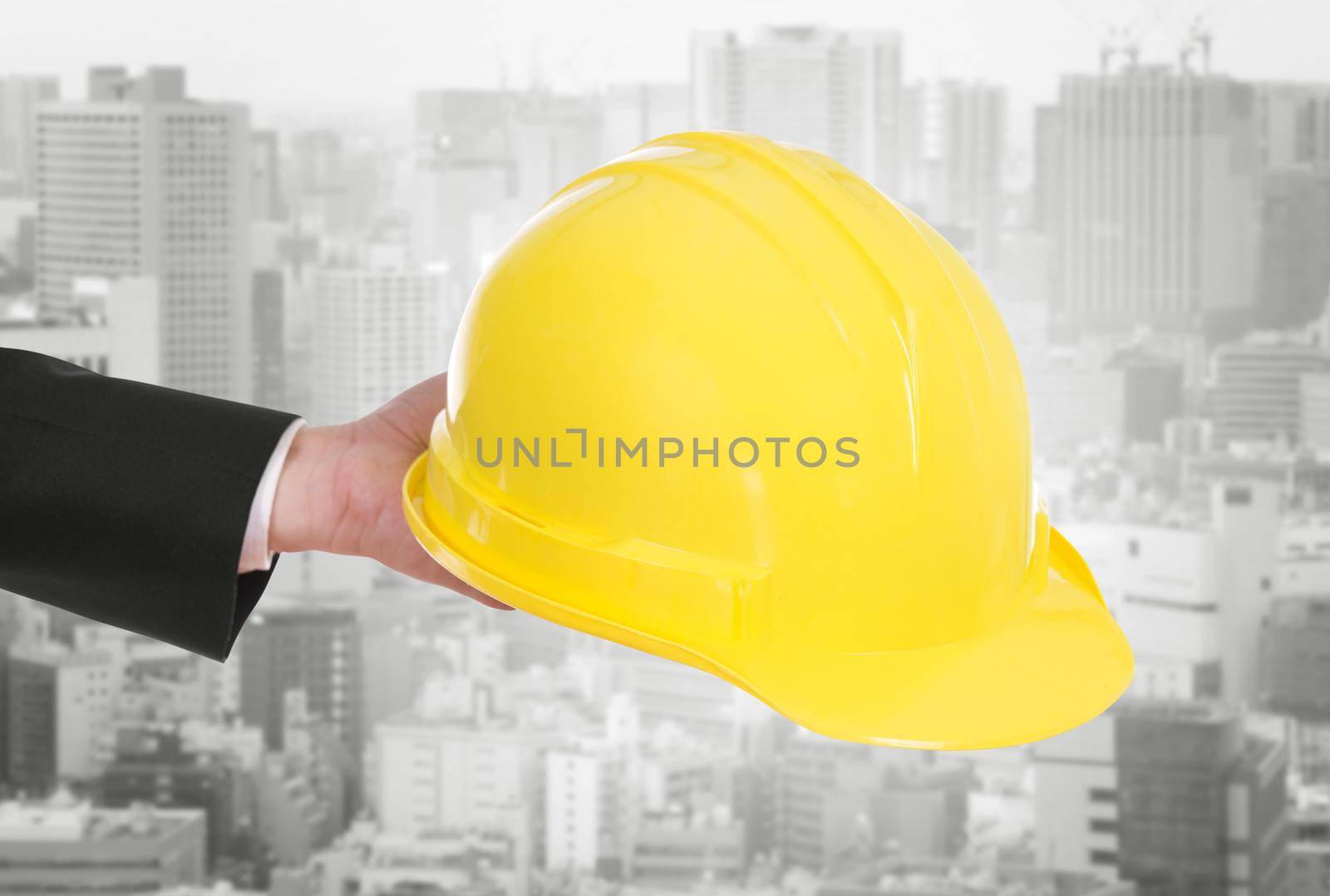 hand of engineer holding yellow helmet with city background