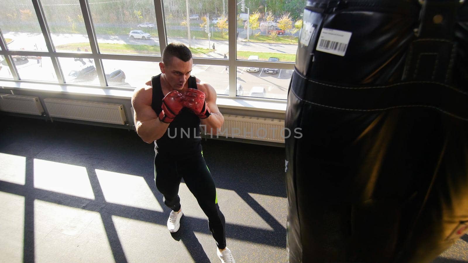 Muscular bodybuilder in training gloves beats a punching bag, looking concentrated