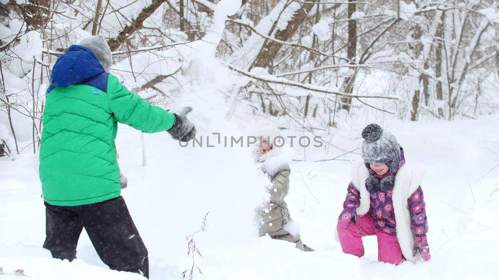 Two little girls playing with a little boy in the snow in winter forest. Mid shot