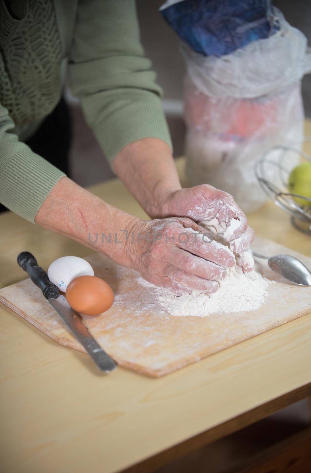 An old lady making little pies. Knead the dough on the desk by Studia72