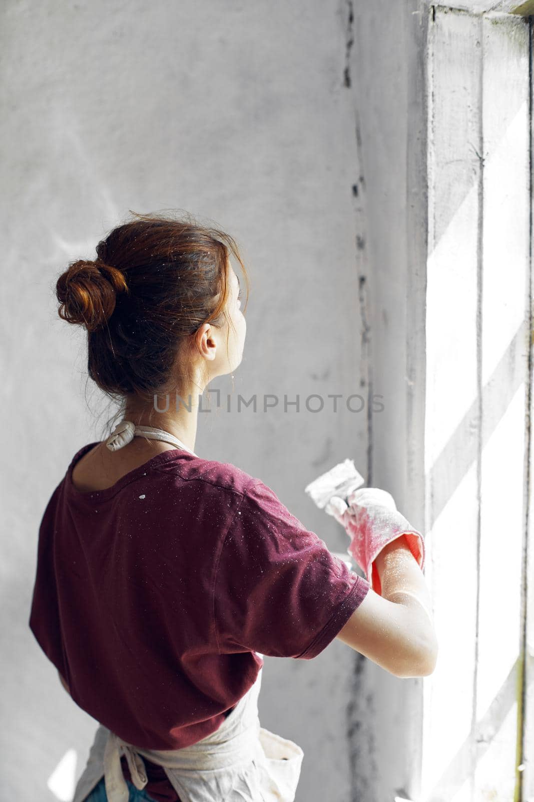 Woman in a white apron paints a window in a house interior renovation by Vichizh