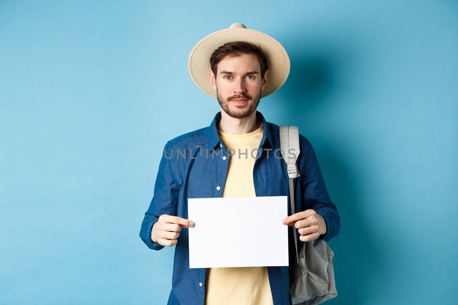 Image of smiling guy in straw hat backpacking, hitchhiking with piece of paper, travelling abroad on summer vacation, blue background by Benzoix