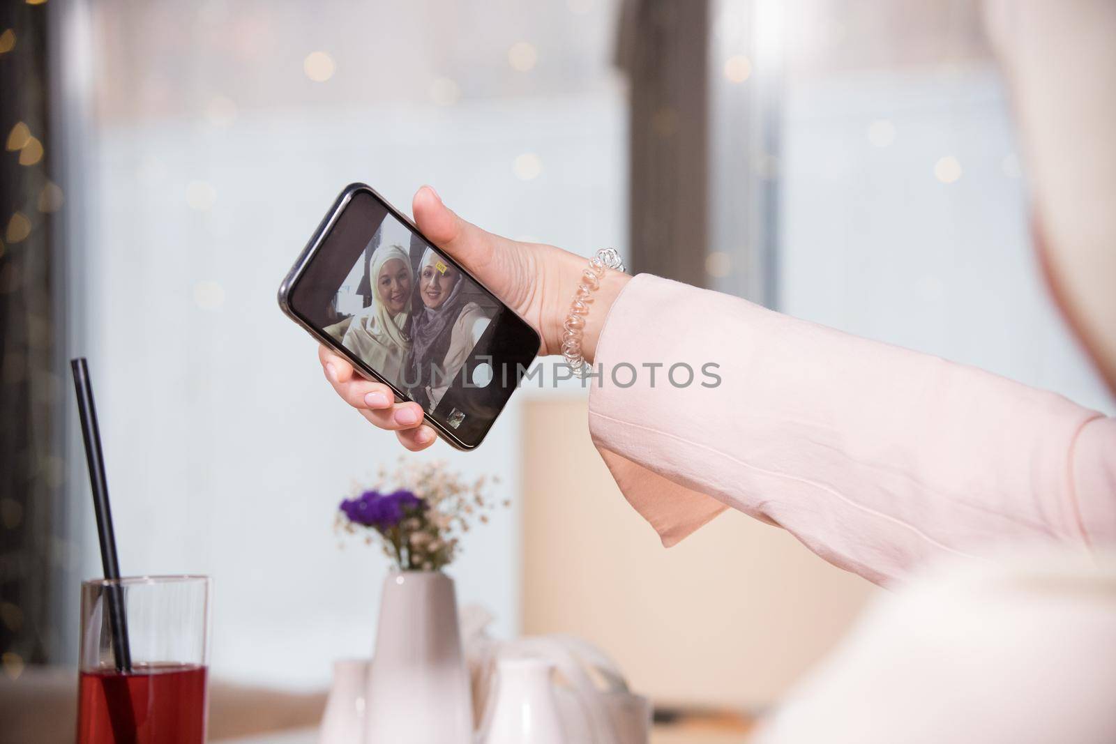Two Muslim women take a selfie at a table in a cafe, telephoto shot