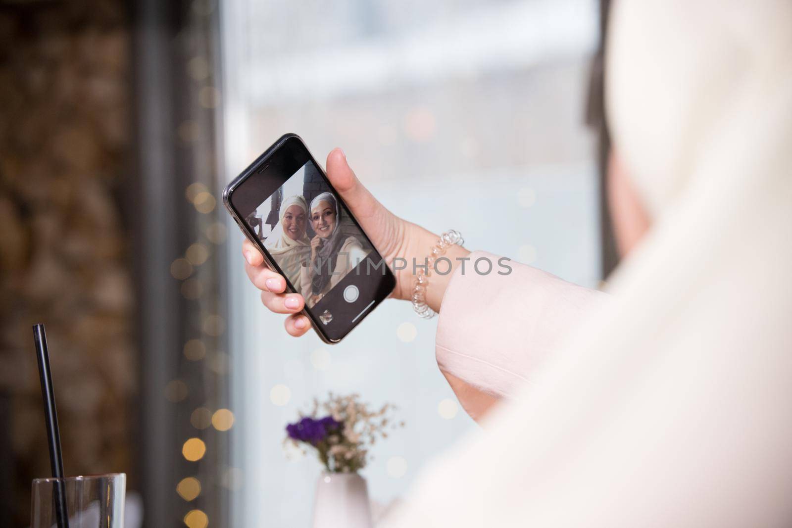 Two young muslim women take a selfie at a table in a cafe, telephoto shot