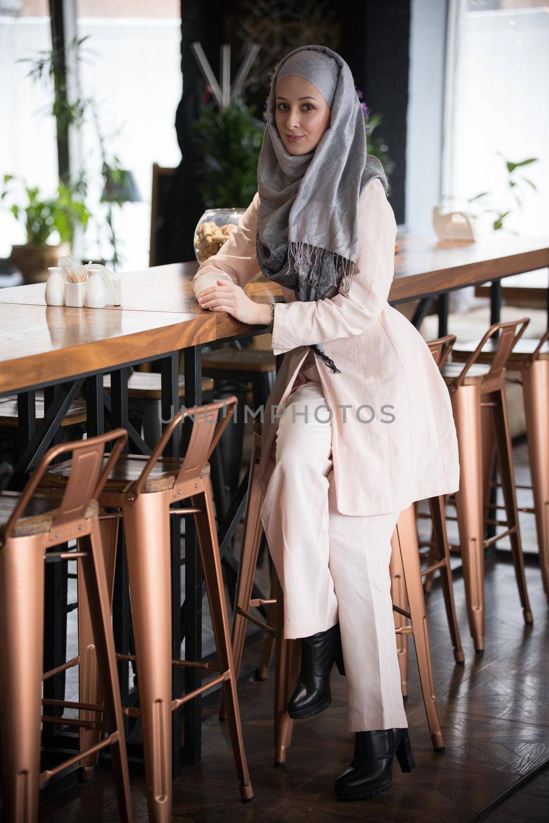 A young muslim woman sitting on a bar chair in a cafe by Studia72