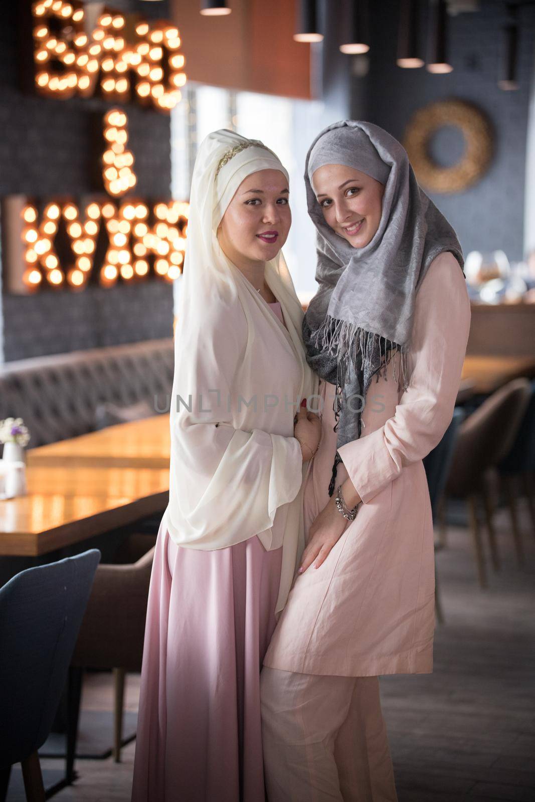Two young muslim smiling women standing in the cafe. Portrait