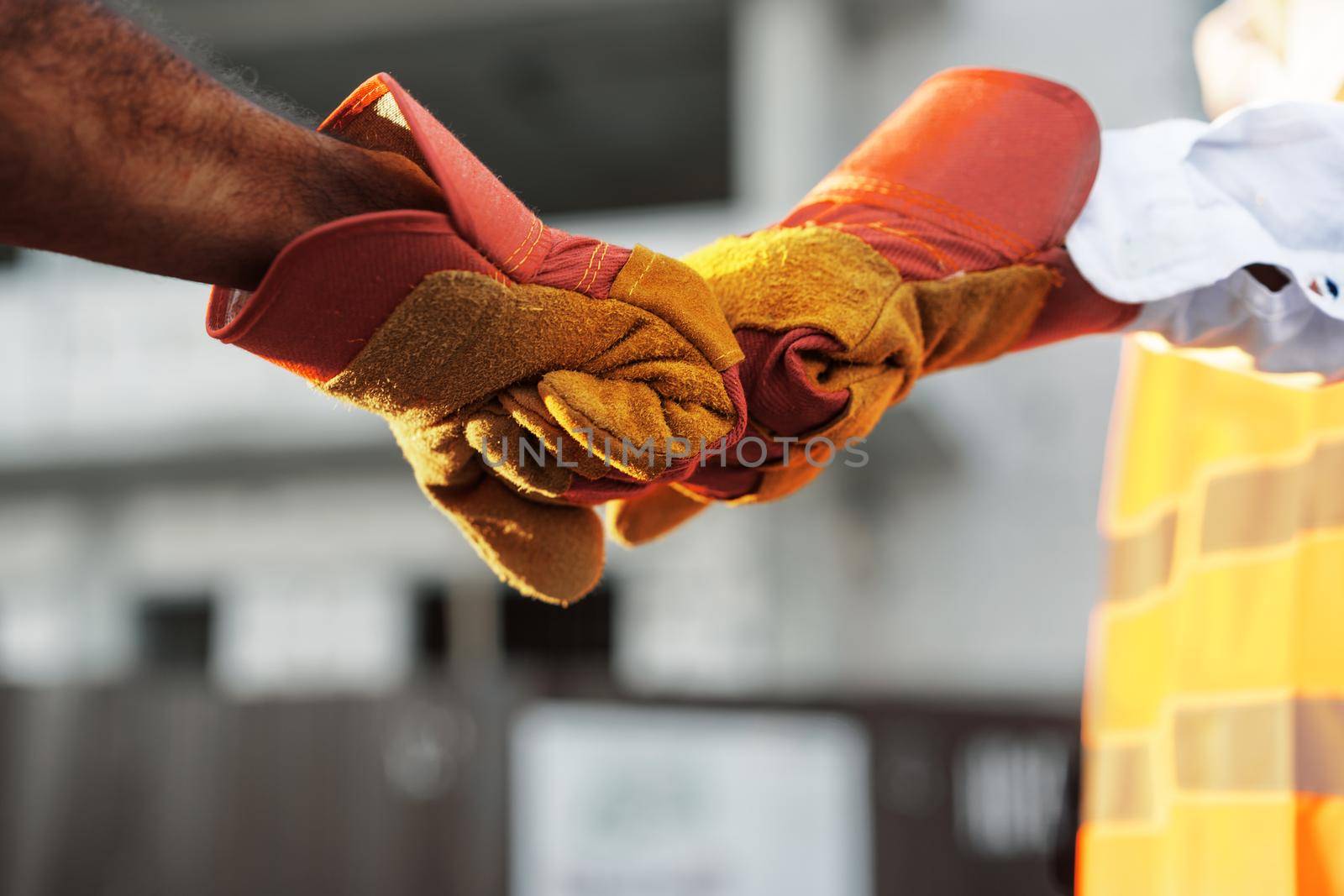 Two men engineers in workwear shaking hands against construction site, close up