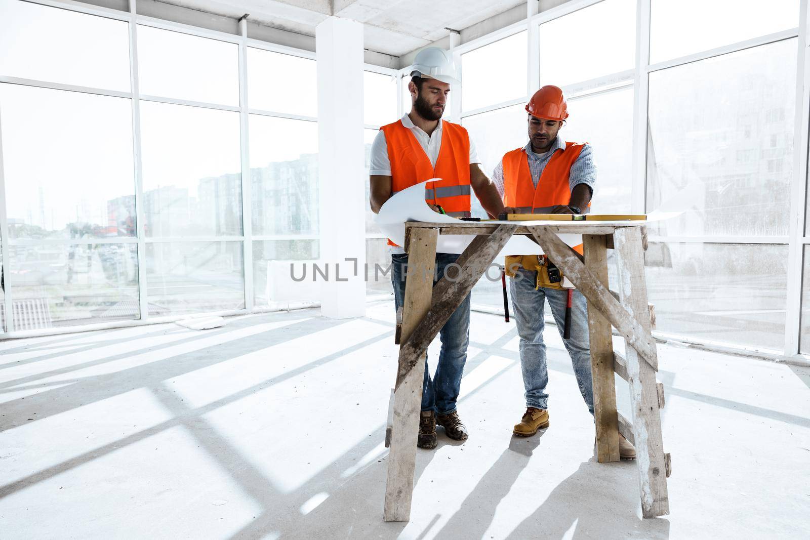 Two young engineers man looking at project plan on the table in construction site