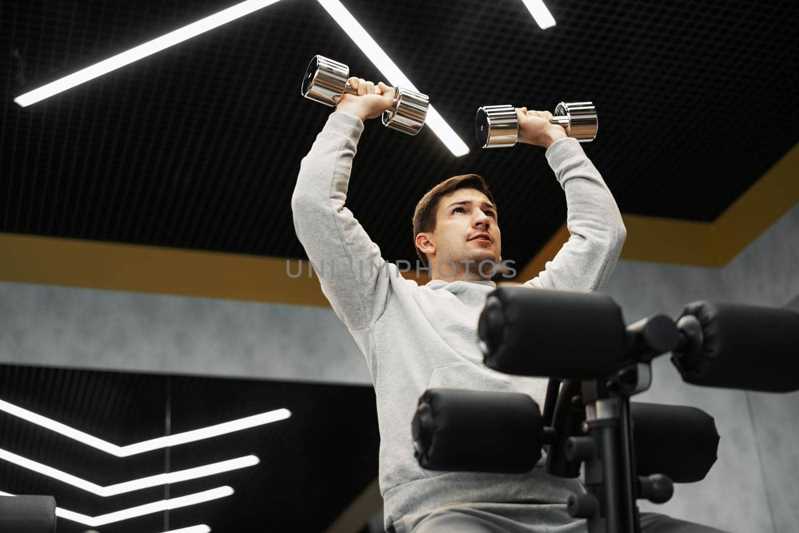Determined handsome young male working out in gym with dumbbells, close up