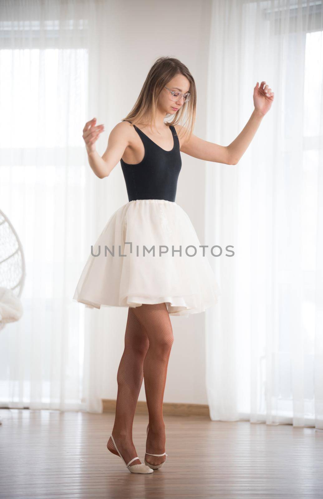 Ballerina in glasses stands on tiptoe in the afternoon in the dance studio by Studia72