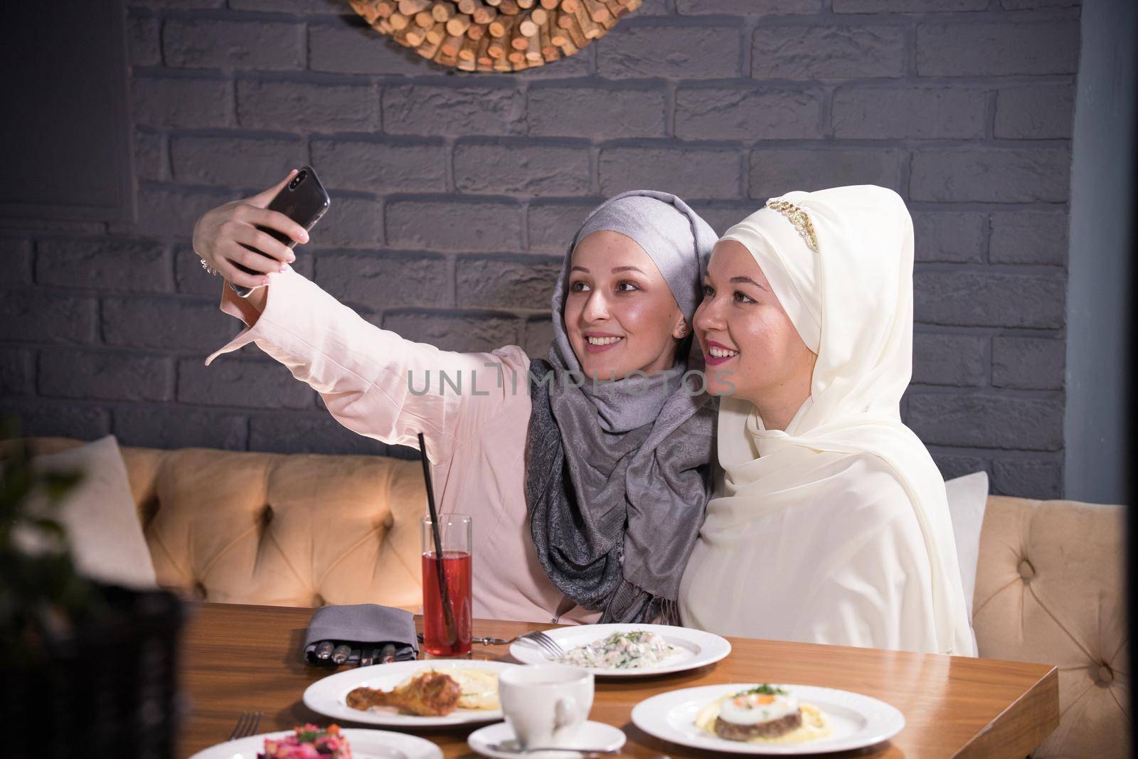 Two Muslim girl take a selfie at a table in a cafe, telephoto shot