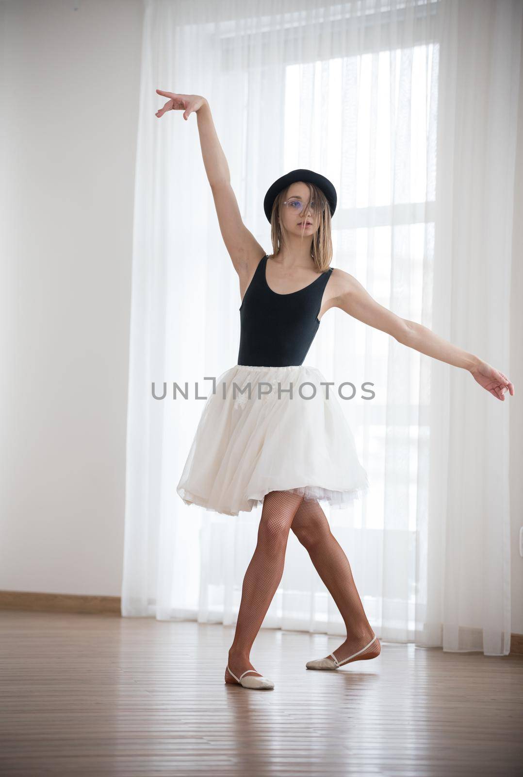 Ballet girl in the hat is dancing in the studio, telephoto shot