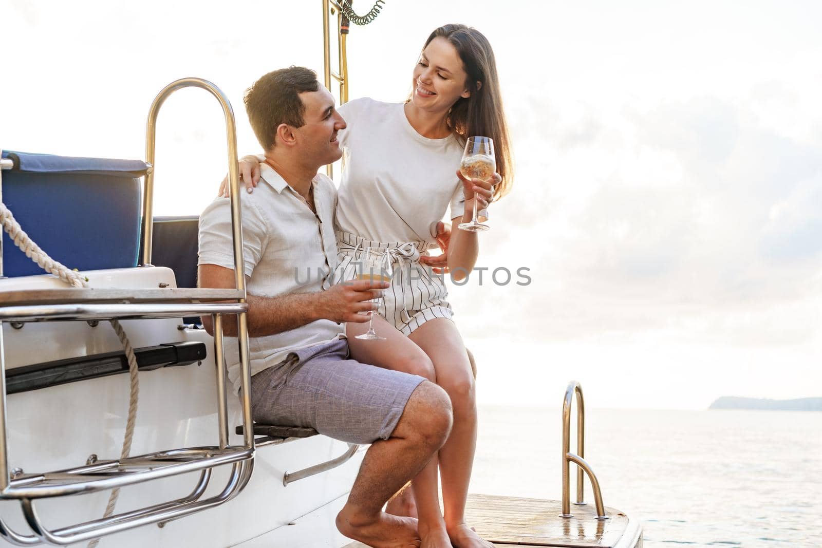 Young loving couple sitting on the yacht deck and drinking wine together