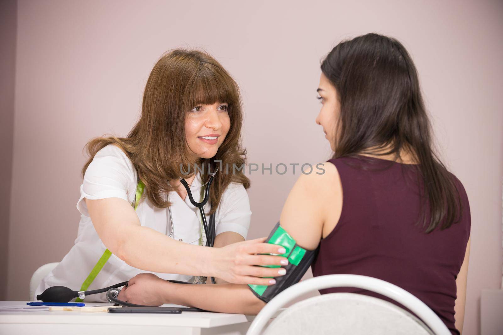 cosmetology beauty clinic. doctor cheking patient's blood pressure, talking to her and holding her hand