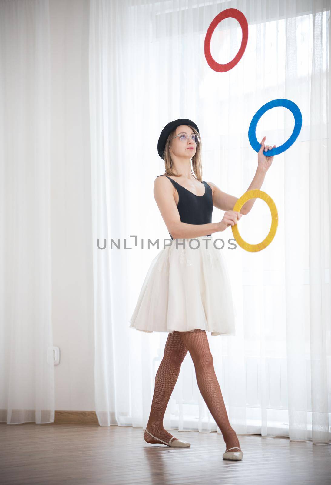 Young woman in a hat juggles with multi-colored rings in the studio, elephoto shot