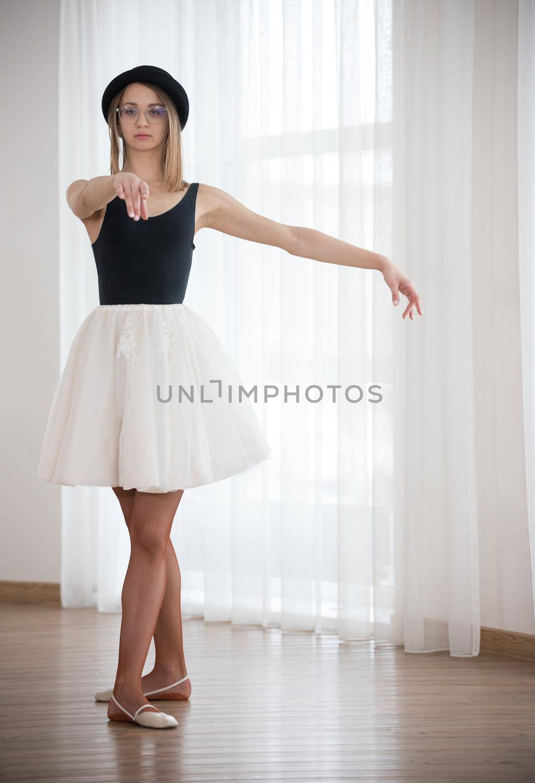 Ballerina in the hat is stretching out her arm forward, in the studio, telephoto shot