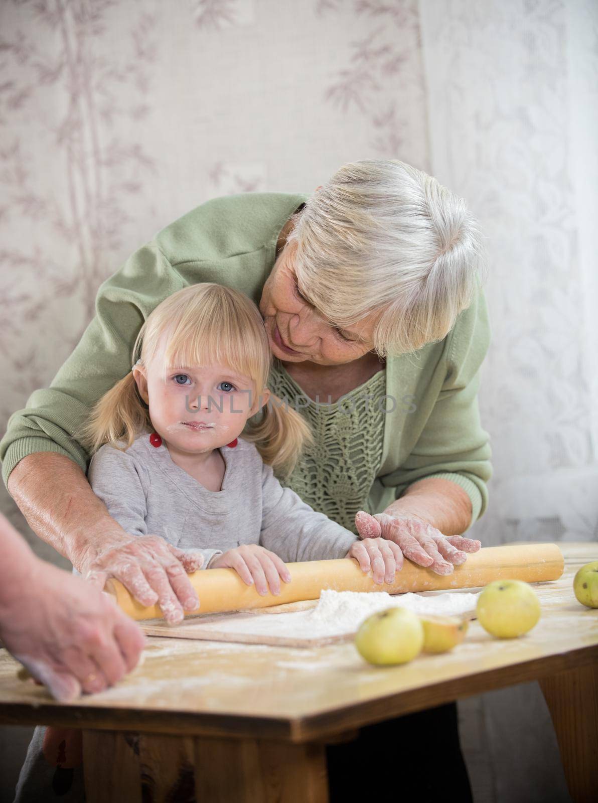 A grandmother making little pies with her granddaughter. Rolling the dough by Studia72