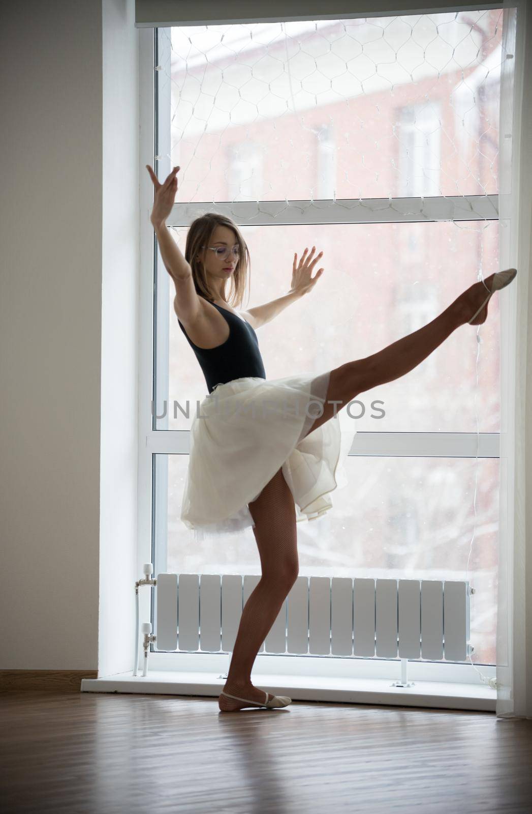 Girl ballerina standing with raised leg in the studio by Studia72