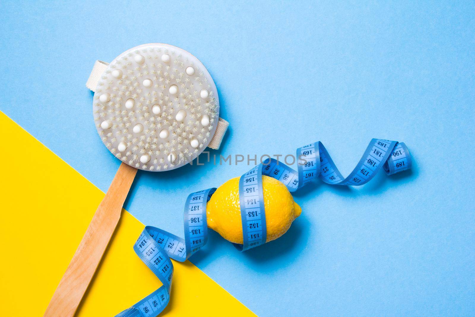blue measuring tape, wooden brush with natural pile of cactus and lemon on a yellow and light blue background copy space top view, anti-cellulite massage concept