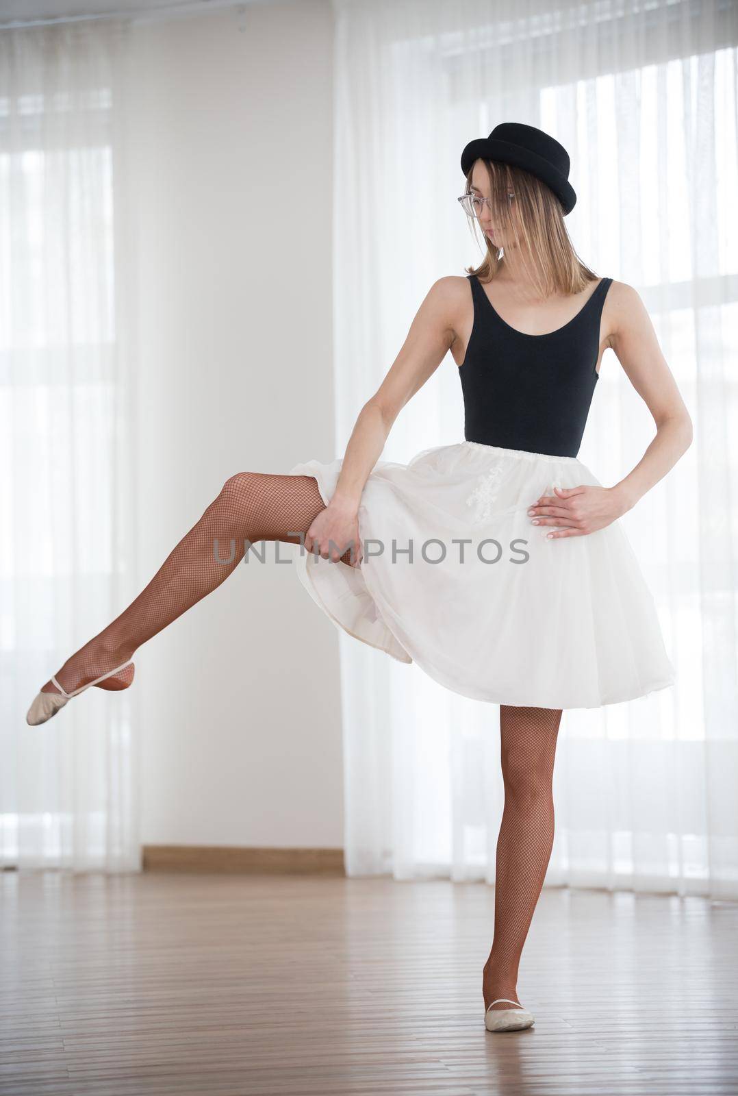 Ballerina in a hat bends a leg to the side, in the studio by Studia72