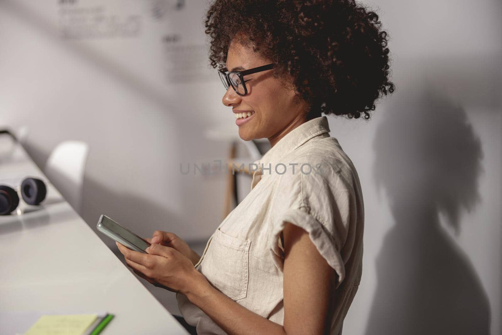Side view of happy Afro American lady in glasses holding smartphone and typing message