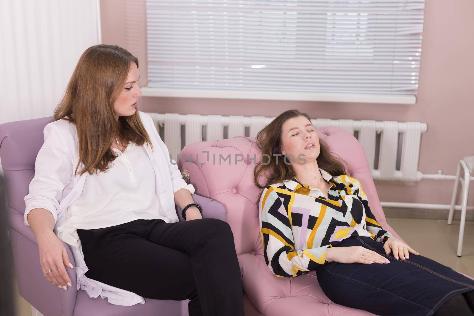 Young woman lying in the chair with closed eyes and talking to the psychologist sitting next to her at the doctor's office by Studia72