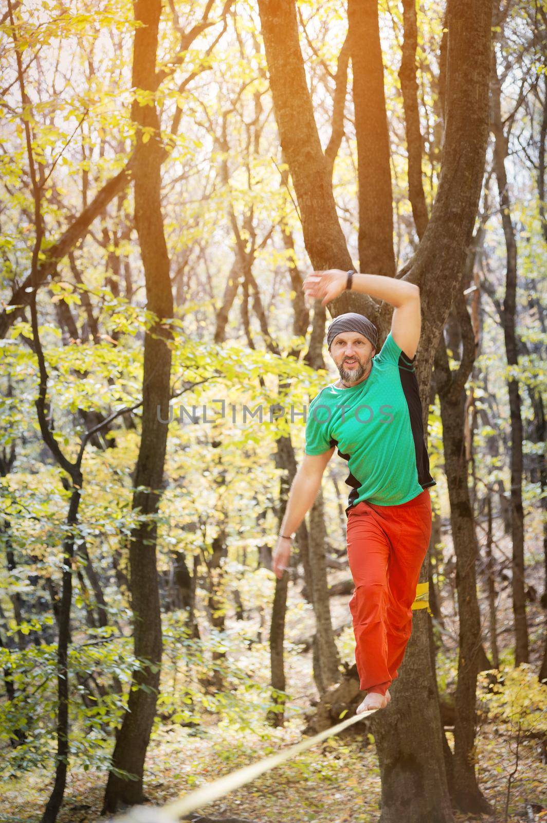 Male tightrope walker balancing barefoot on slackline in autumn forest. The concept of outdoor sports and active life of people aged by yanik88